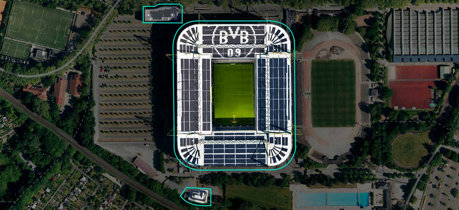 Aerial view of a football stadium with solar panels on the roof and surrounding sports fields.