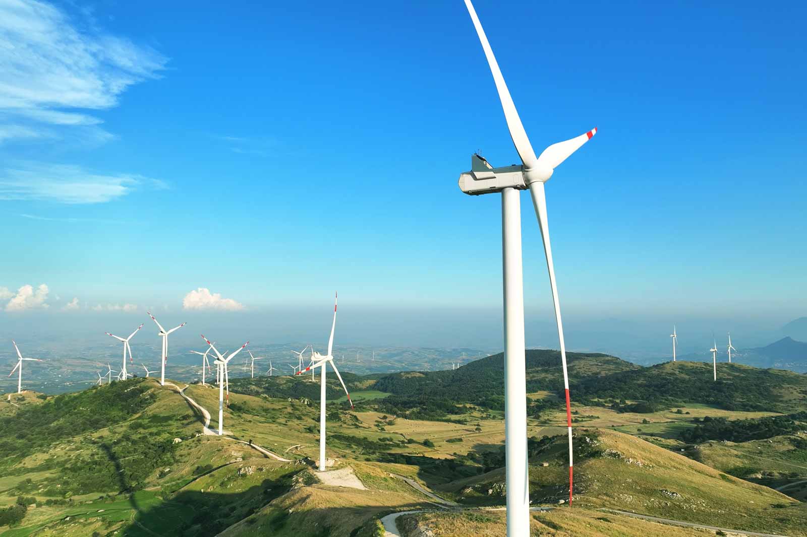 A wind turbine on a hill with several more turbines in the distance under a clear blue sky.
