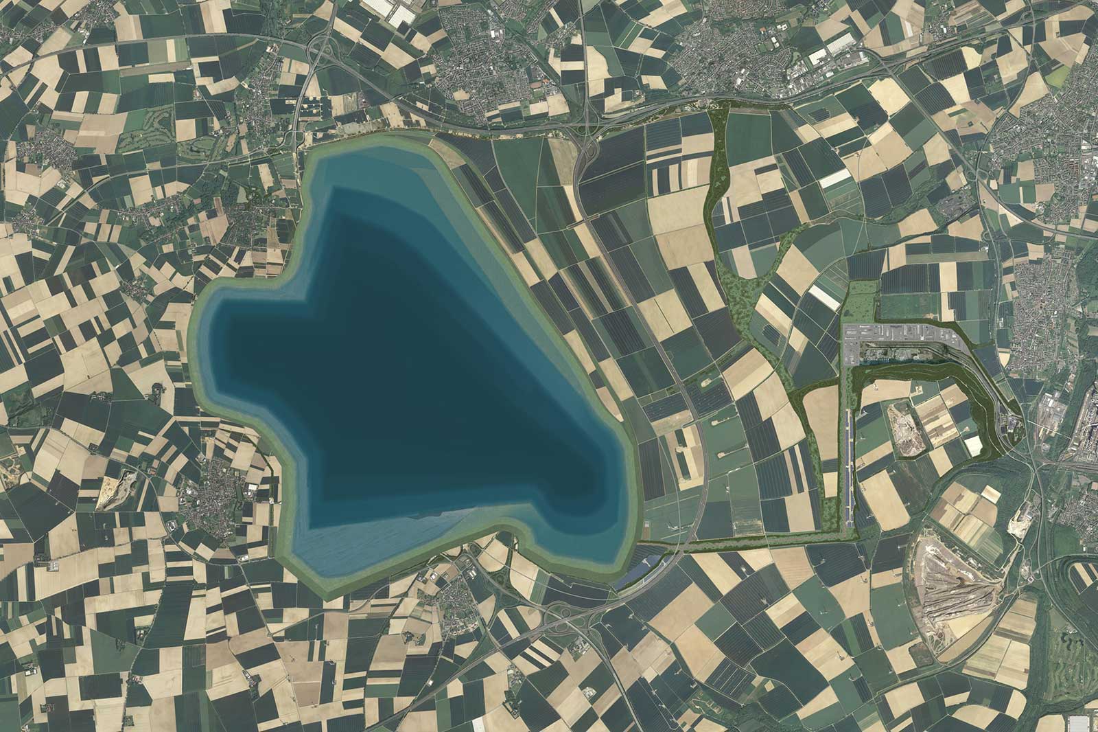 Eine Vogelperspektive auf einen See, umgeben von patchworkartigen Feldern und Straßen in einer ländlichen Landschaft.