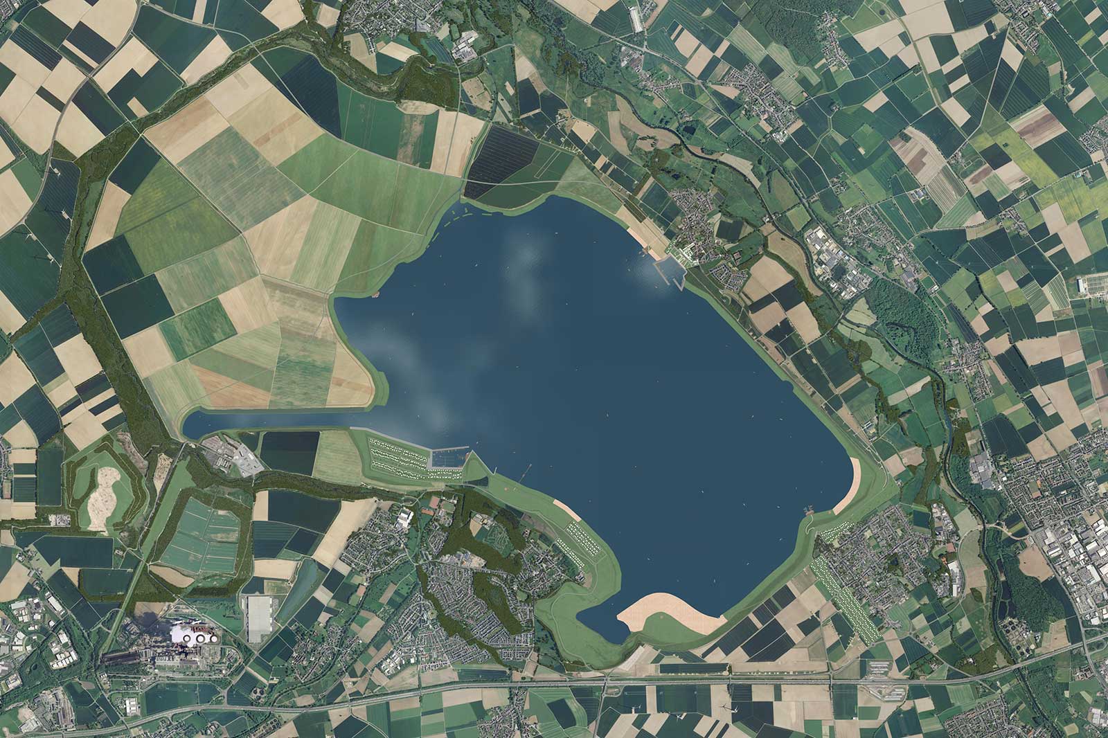 Eine Luftaufnahme eines großen Sees, umgeben von Feldern in Patchwork-Optik und kleinen Siedlungen, mit sichtbaren Straßen und Bäumen.