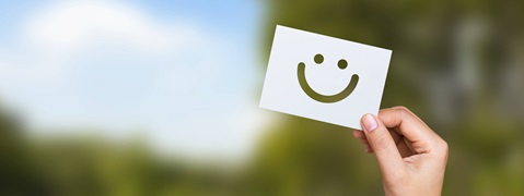 A hand holding a card with a smiling face against a blurred green background.