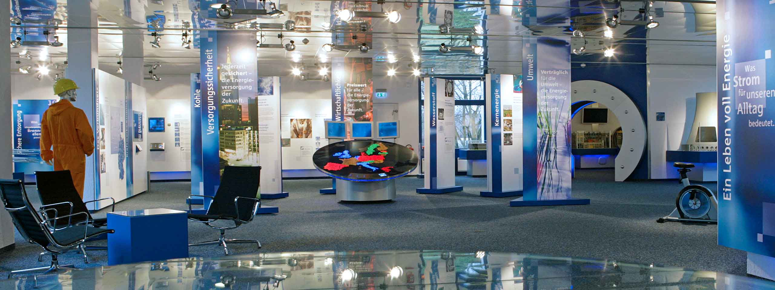 Ein modernes Ausstellungsdesign mit blauen Wänden, Informationspanels und einem interaktiven Kartenanordnungserdisplay.