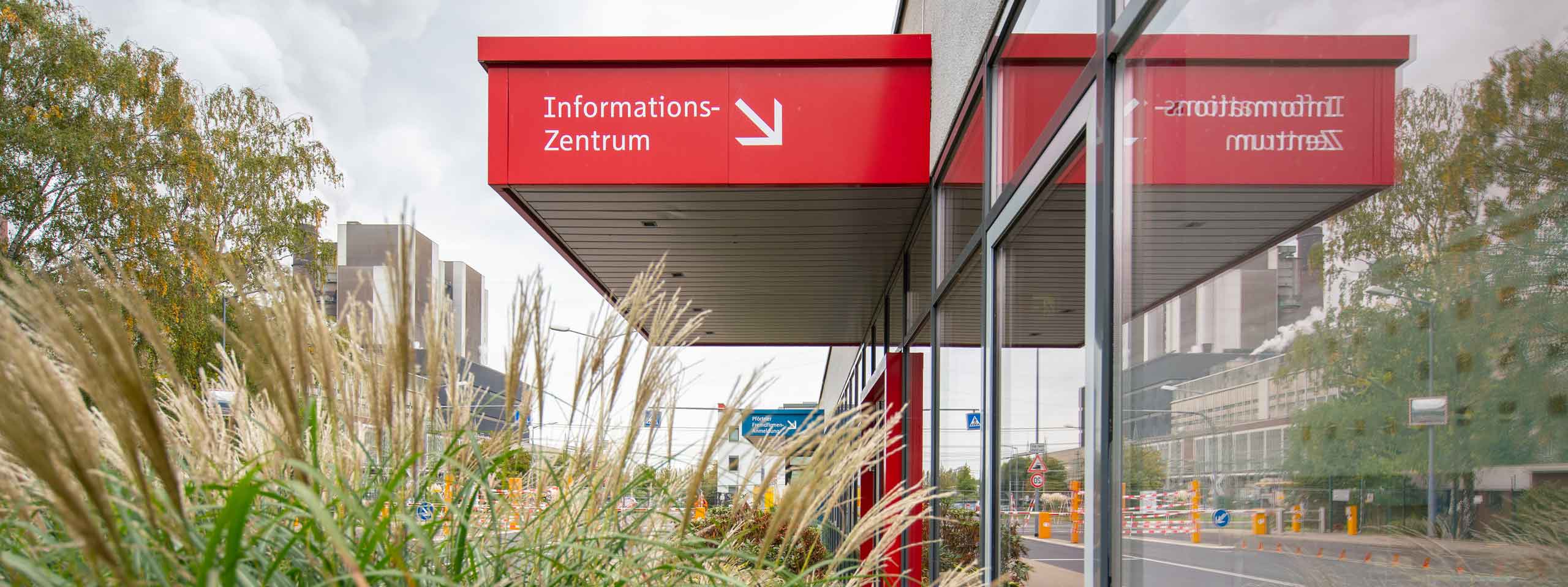 Das Informationszentrum ist in kräftigem Rot markiert, umgeben von Gras und Bäumen, mit einem modernen Stadtbild im Hintergrund.