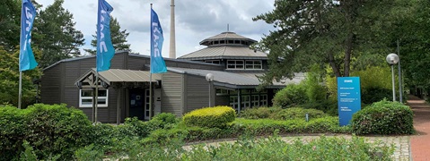 Ein Informationszentrum mit umgebender grüner Vegetation, Fahnen und einem Gehweg in einer natürlichen Umgebung.