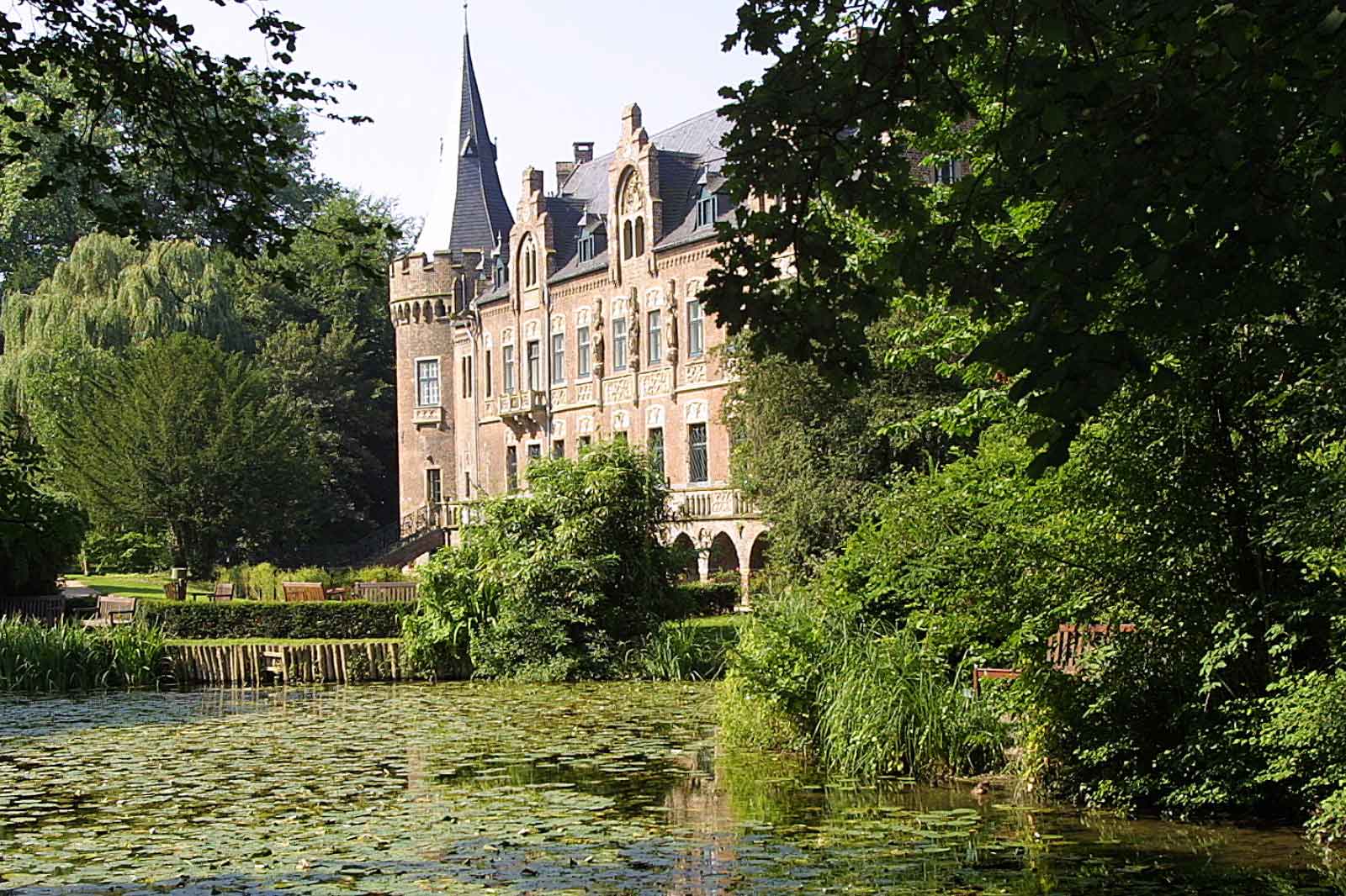 Ein malerisches Schloss, umgeben von üppigem Grün und einem ruhigen Teich, der mit Seerosen bedeckt ist.