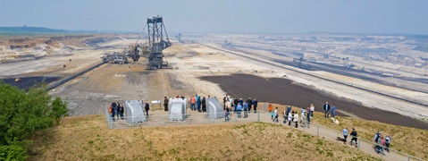 Eine Gruppe von Menschen steht an einem Aussichtspunkt über eine große Tagebau-Landschaft mit Maschinen im Hintergrund.