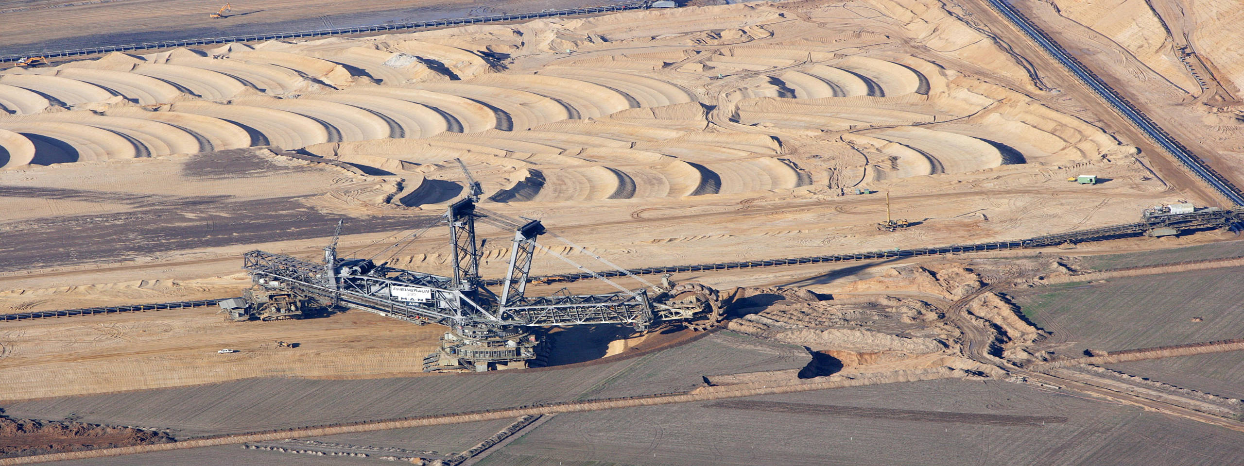 Eine Luftaufnahme eines großen Tagebaus mit einem Bagger und nebligen Sandhügeln im Hintergrund.