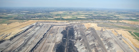 Luftaufnahme eines großen Tagebaus mit abgetragenem Boden, Abraumhalden und umliegender Landschaft.