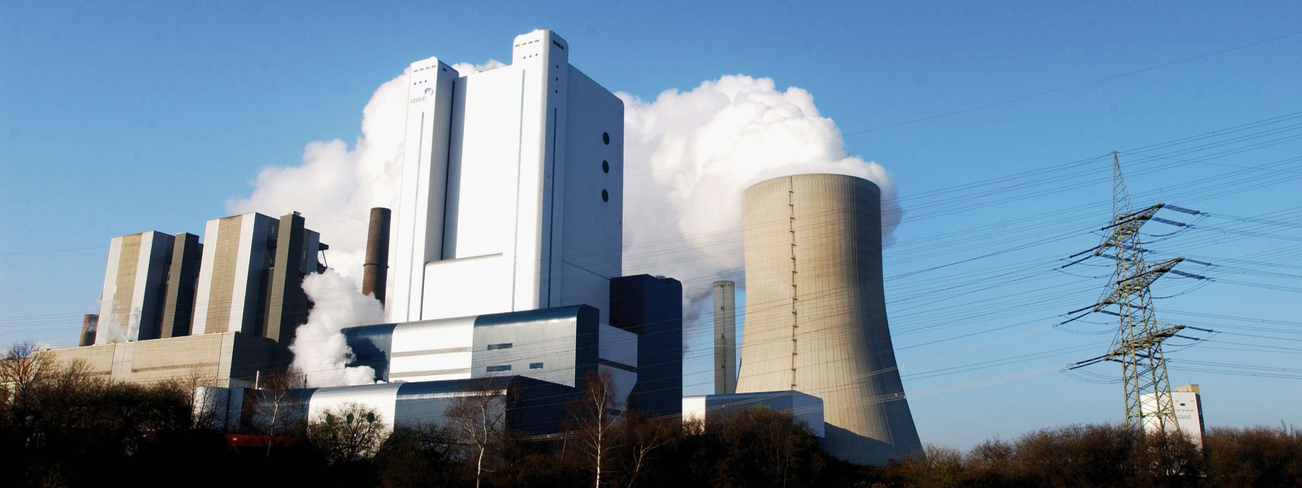 Ein Kraftwerk mit großen Kühltürmen und aufsteigendem Dampf vor einem klaren blauen Himmel.