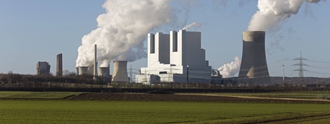 Kraftwerk mit rauchenden Kühltürmen und grünen Feldern im Vordergrund.