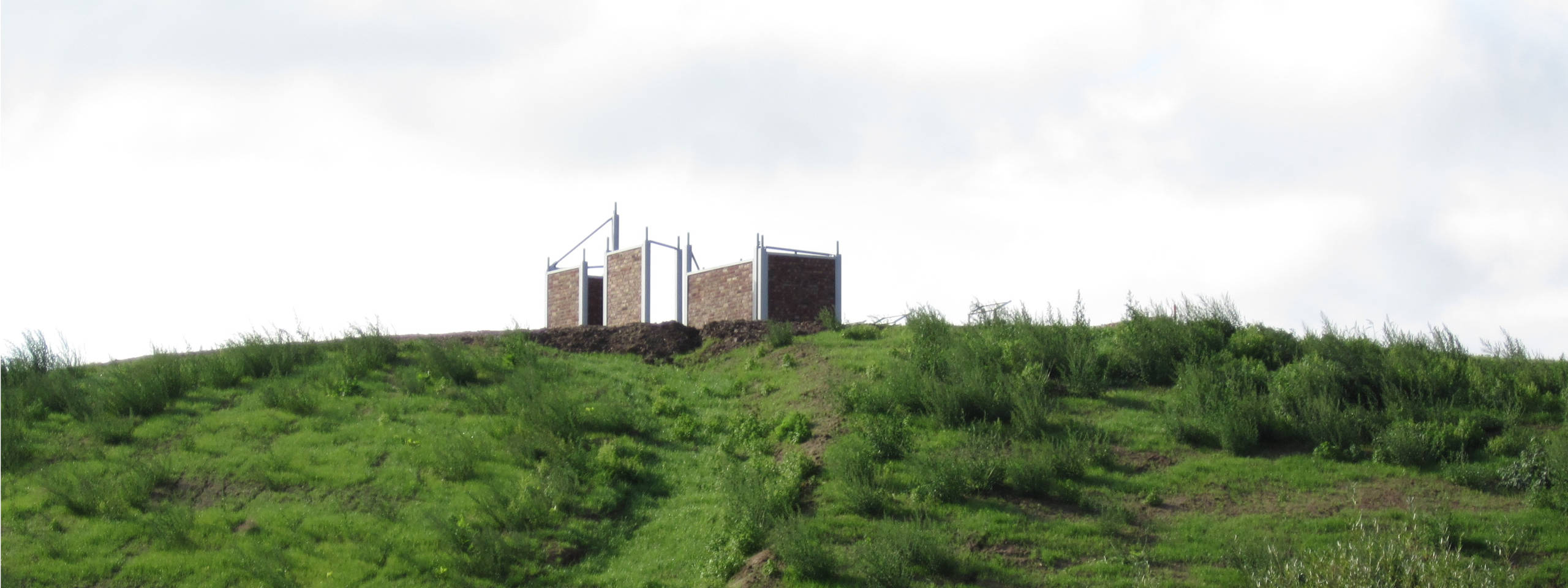 Drei Mauern aus Ziegeln stehen auf einem grünen Hügel unter einem bewölkten Himmel.