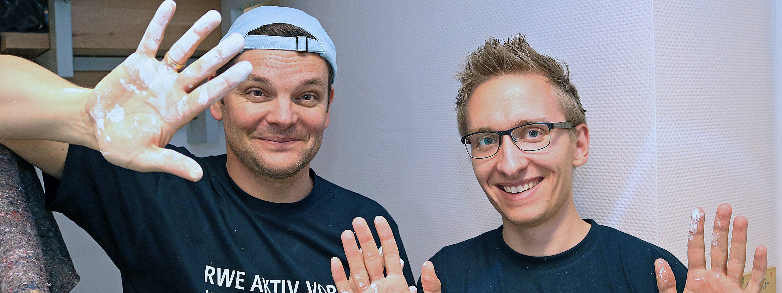 Zwei Personen mit beschichteten Händen, die in einem Raum stehen und die Hände hochheben.