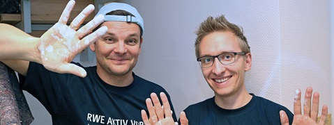 Zwei Personen mit beschichteten Händen, die in einem Raum stehen und die Hände hochheben.