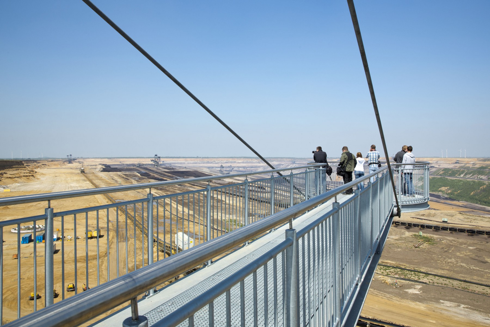Eine Luftaufnahme eines massiven Baggers mit einem langen Förderband in einem Feld, umgeben von Protestierenden und Fahrzeugen auf einer Straße.