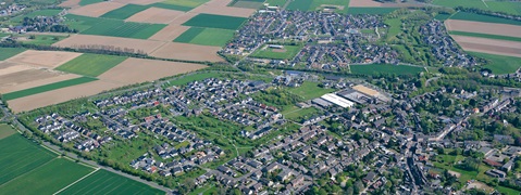 Eine Luftaufnahme eines Wohngebiets mit grünen Feldern und Häusern, die eine Mischung aus Natur und Vorstadtleben zeigen.