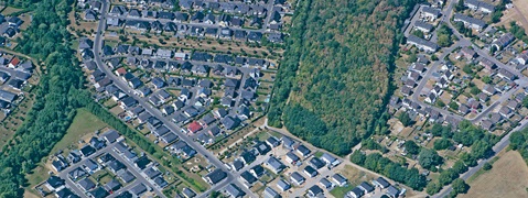 Luftaufnahme einer Wohngegend mit Häusern und einem nahegelegenen Waldstück.