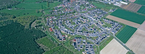 Luftaufnahme eines Wohngebiets, umgeben von Feldern und Wäldern, zeigt eine gut geplante Anordnung von Häusern.