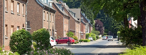 Eine ruhige Straße mit Backsteinhäusern, grünen Bäumen und Fahrzeugen, die entlang der Straße parken.