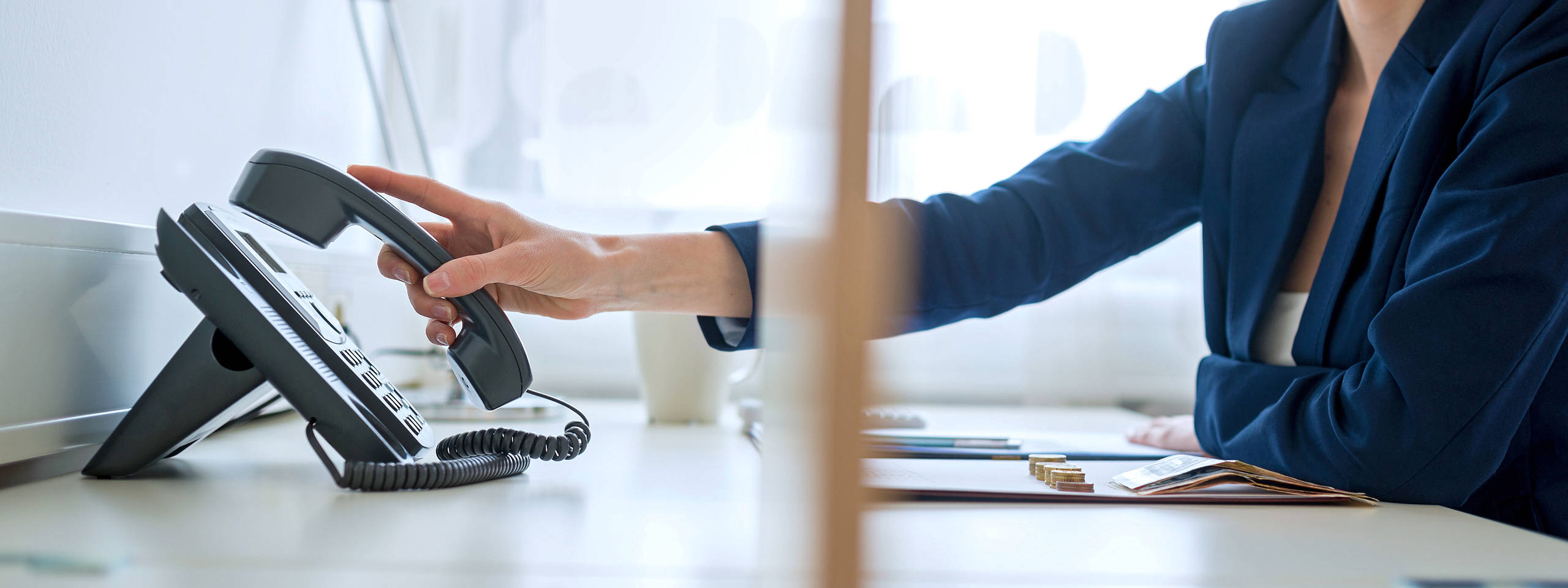 Eine Person hebt den Hörer eines Telefons an einem Schreibtisch mit Schreibutensilien und Geld auf.