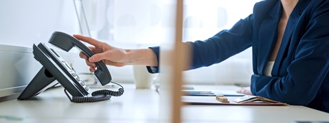 Eine Person hebt den Hörer eines Telefons an einem Schreibtisch mit Schreibutensilien und Geld auf.