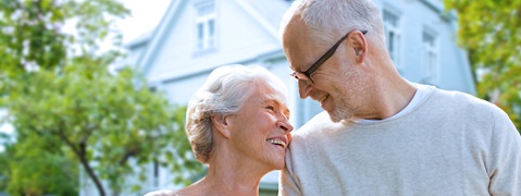 Ein älteres Paar steht im Freien, umgeben von grünen Bäumen und einem hellen Hintergrund, in einem freundlichen Moment.