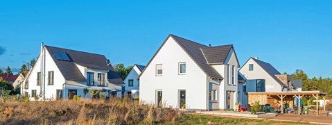 Moderne, weiße Häuser mit dunklen Dächern stehen in einer ruhigen Nachbarschaft. Grünflächen umgeben die Gebäude.