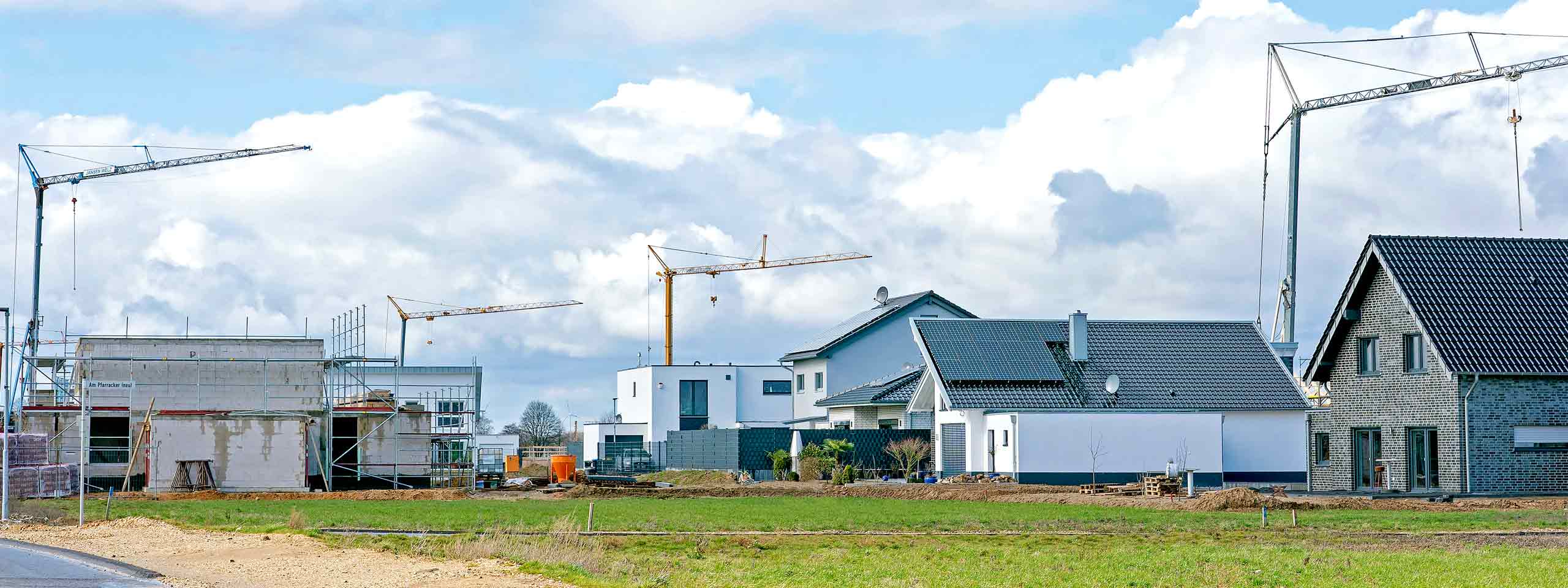 Baugebiet mit Kränen, neuen Häusern und Baustellen, unter einem bewölkten Himmel.