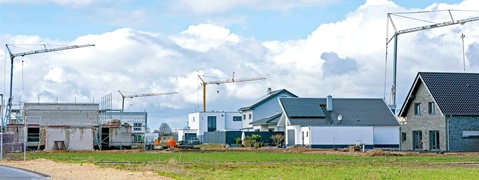 Baugebiet mit Kränen, neuen Häusern und Baustellen, unter einem bewölkten Himmel.