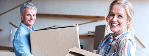 Zwei Personen tragen Kartons in einem modernen Raum mit Holzregalen im Hintergrund.