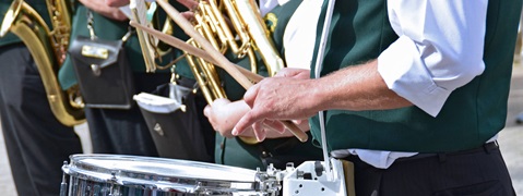 Musiker in grünen Westen spielen Trompete und Schlagzeug während einer Aufführung im Freien.