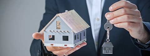 Ein Mann hält ein Modellhaus in der einen Hand und einen Schlüsselanhänger in Form eines Hauses in der anderen Hand.