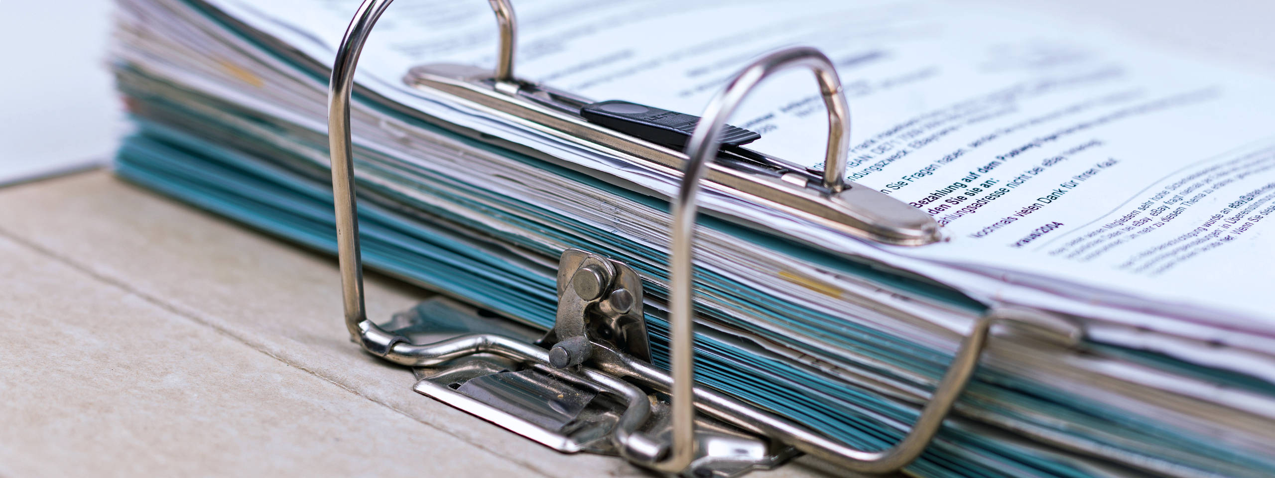 Ein großer Ordner mit bunten Dokumenten und einem Klammerhefter auf einem Tisch.