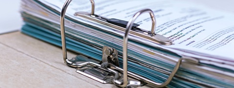 Ein großer Ordner mit bunten Dokumenten und einem Klammerhefter auf einem Tisch.