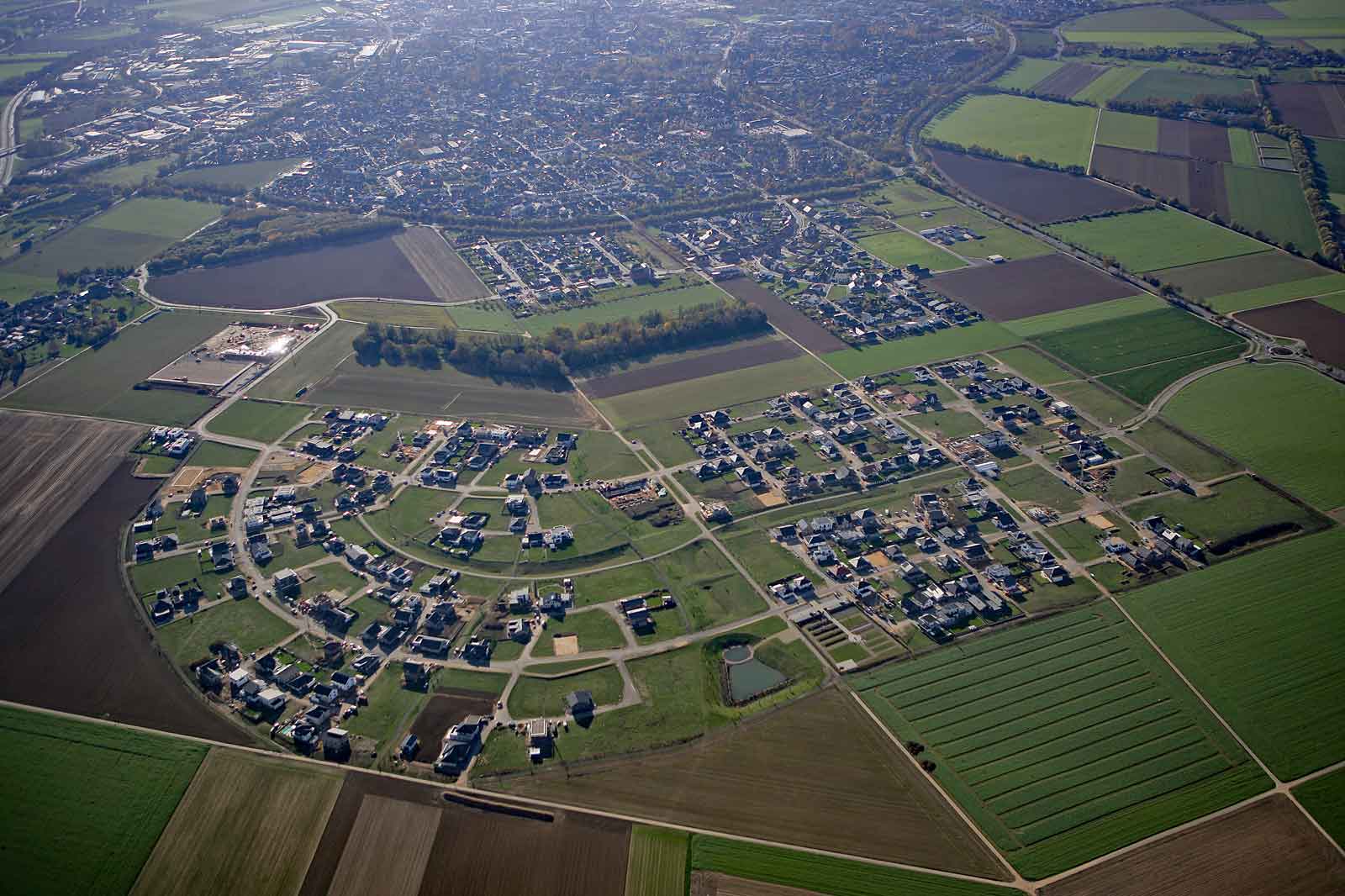 Luftaufnahme eines Wohngebiets mit modernen Häusern und umliegenden Feldern.