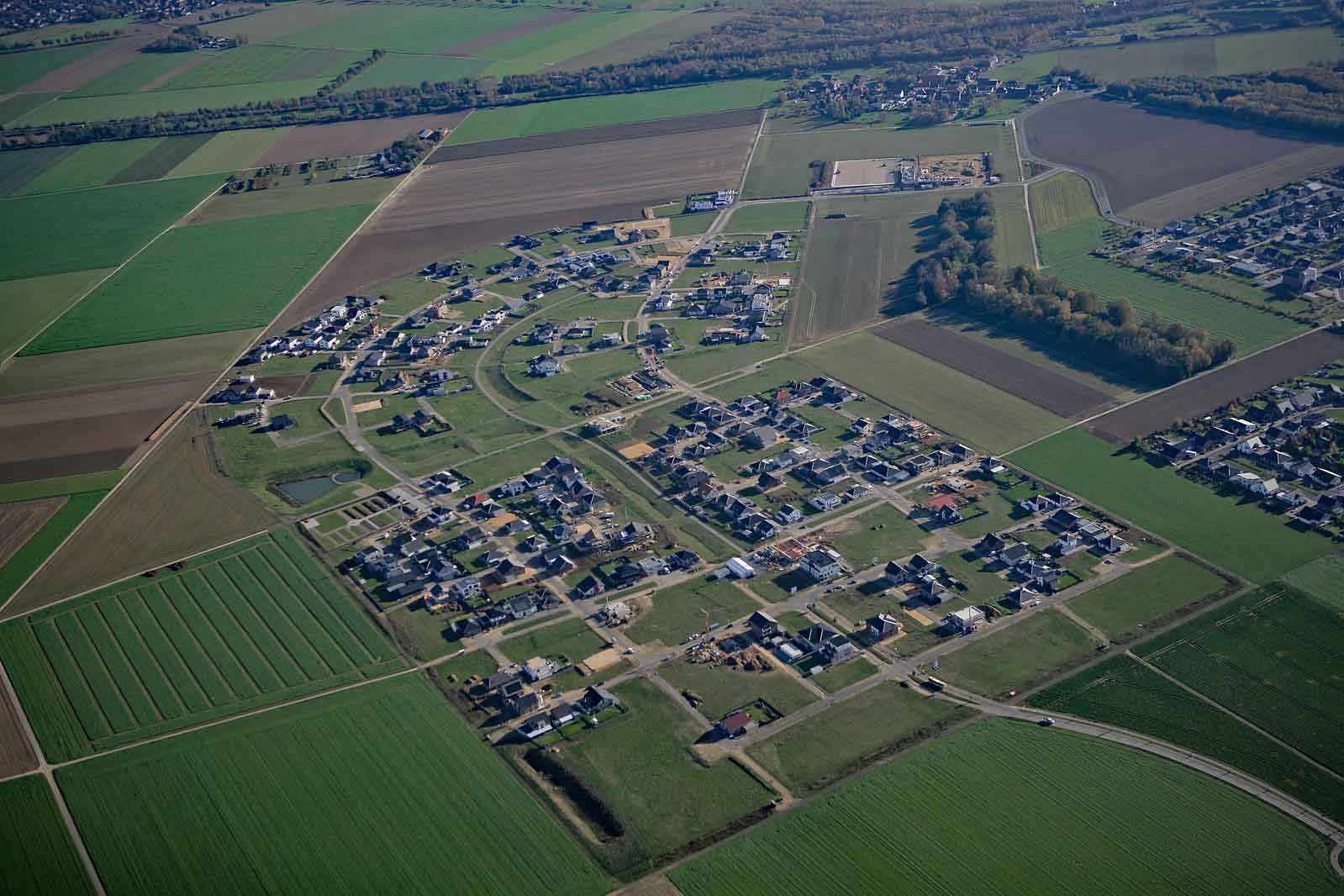 Eine Luftaufnahme einer ländlichen Gemeinde mit Häusern, Feldern und Straßen, umgeben von grünen Landschaften.