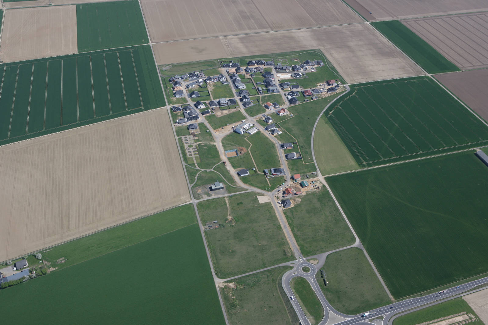 Luftaufnahme eines Neubaugebiets umgeben von Ackerland und grünen Feldern.