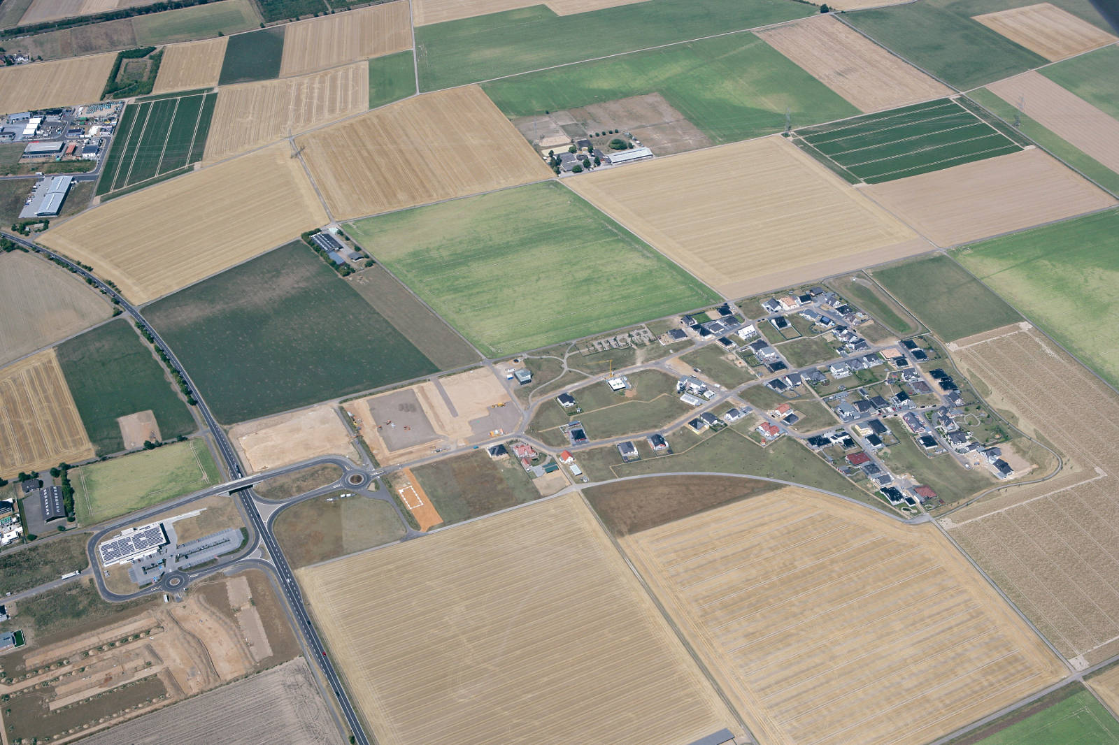 Luftaufnahme einer ländlichen Gegend mit Feldern, Straßen und einem kleinen Dorf.