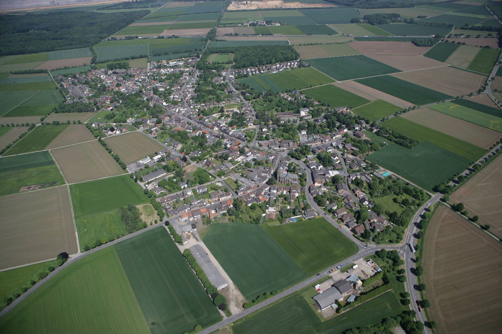 Luftaufnahme eines kleinen Dorfes umgeben von landwirtschaftlich genutzten Feldern und Wäldern.
