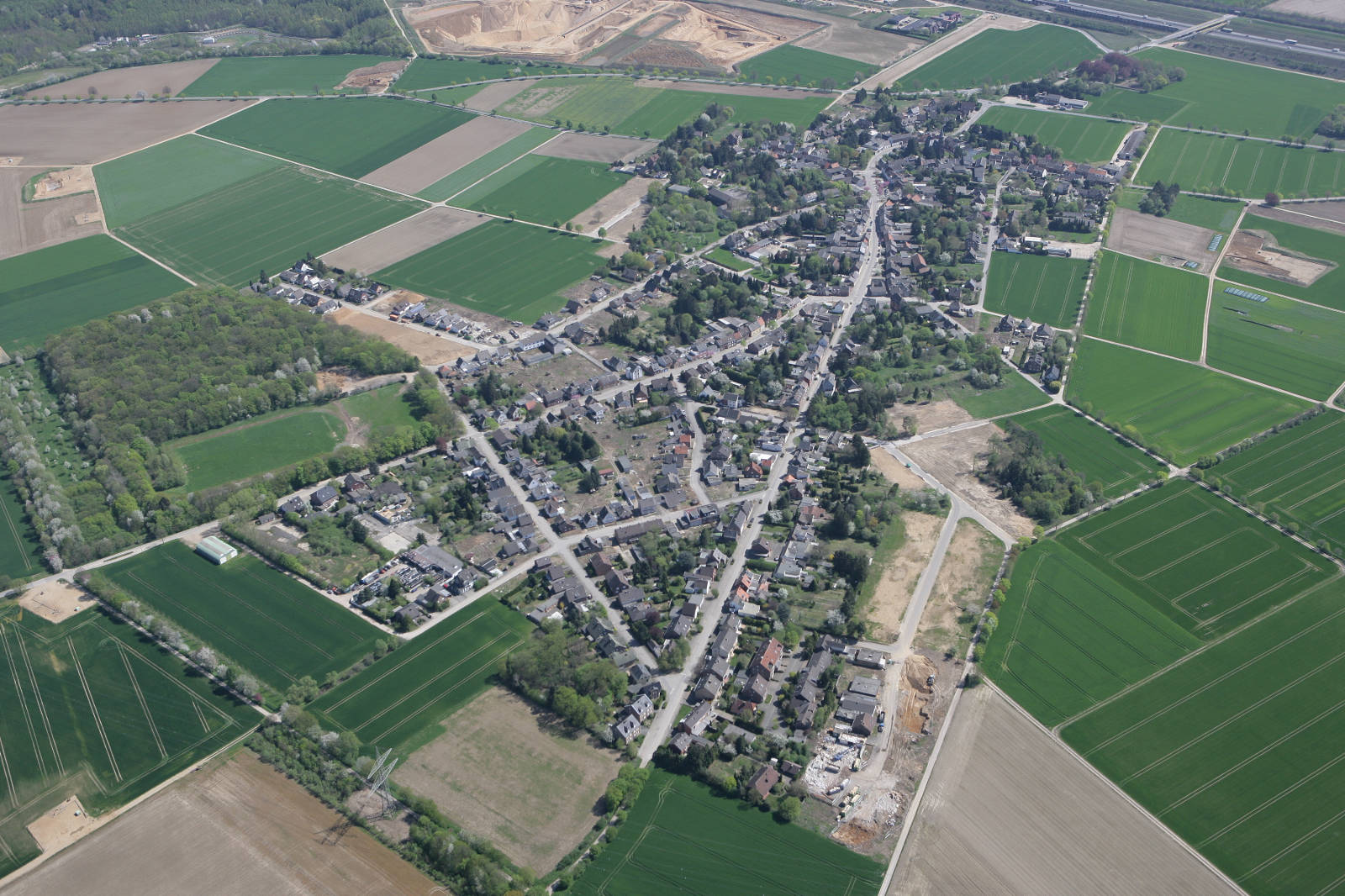 Luftaufnahme eines ländlichen Dorfes, umgeben von üppigen grünen Feldern und Ackerland.