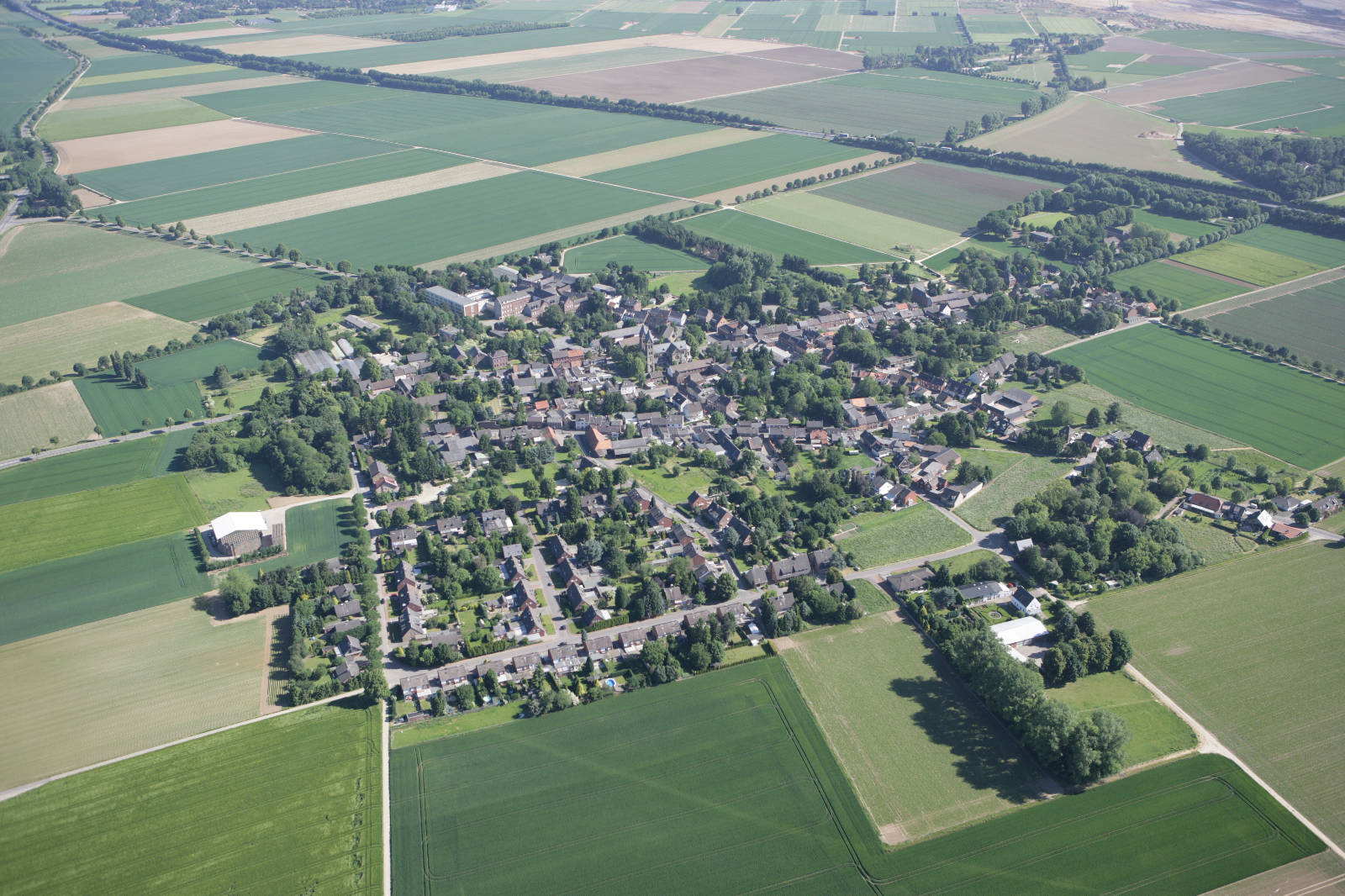 Luftaufnahme einer kleinen Stadt umgeben von landwirtschaftlich genutzten Feldern in verschiedenen Grüntönen.