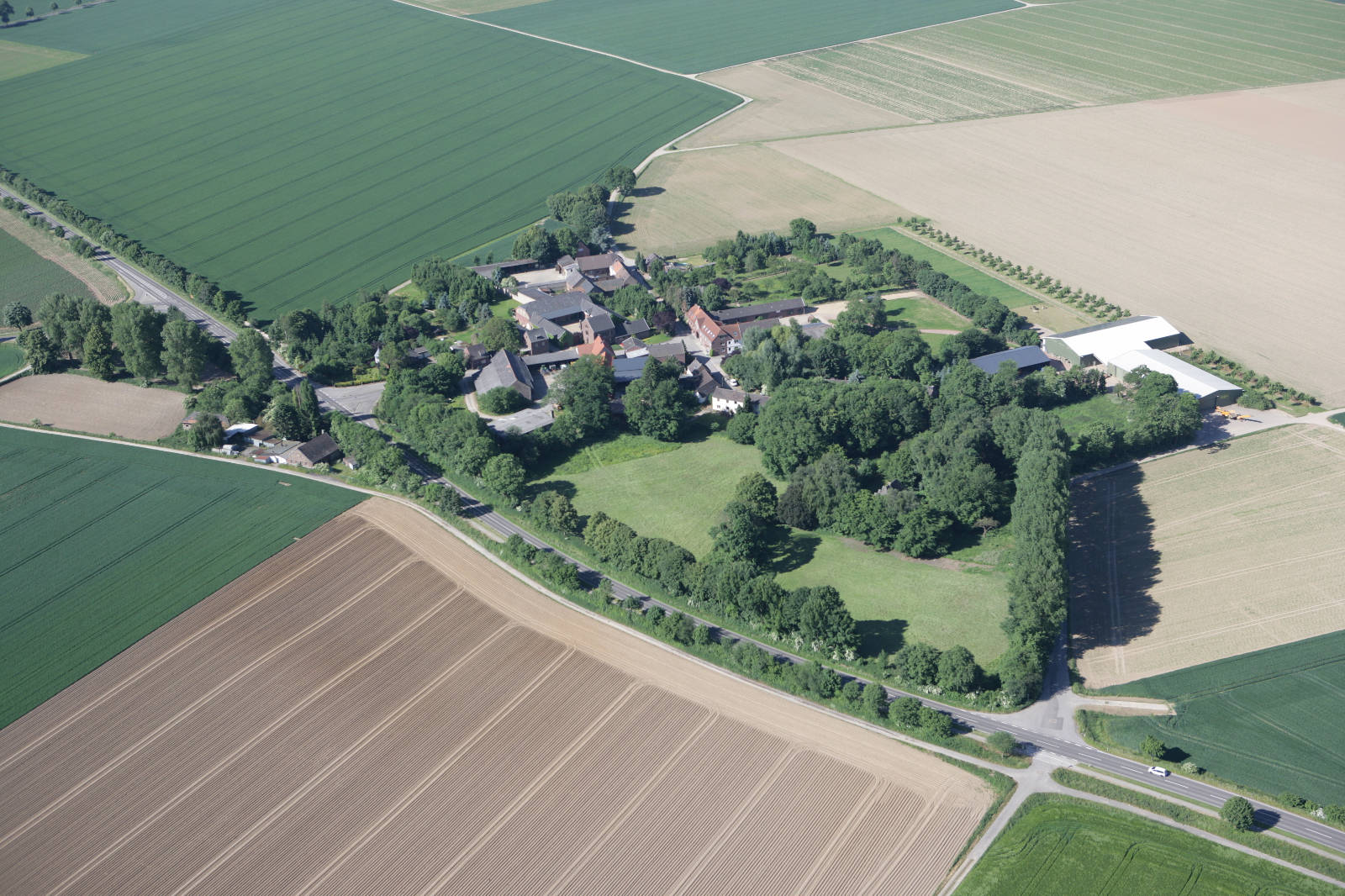 Luftaufnahme eines kleinen Dorfes umgeben von landwirtschaftlichen Feldern und Bäumen.