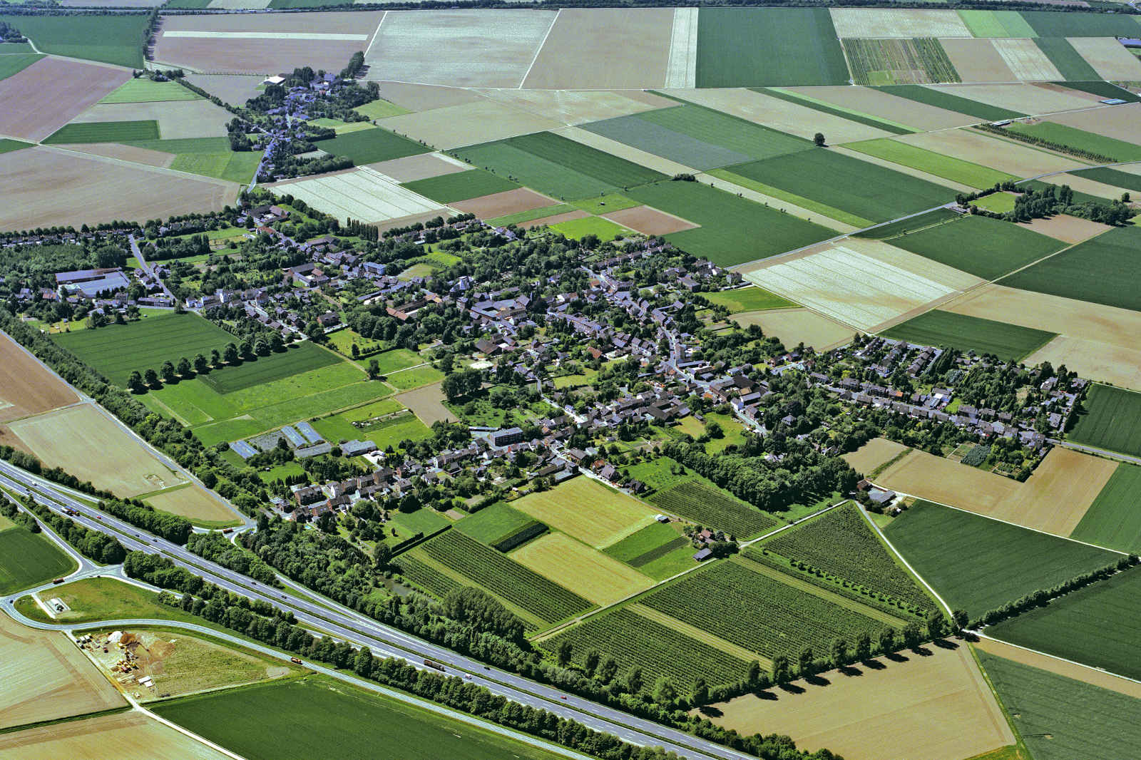 Luftaufnahme eines kleinen Dorfes umgeben von Feldern und landwirtschaftlichen Flächen.