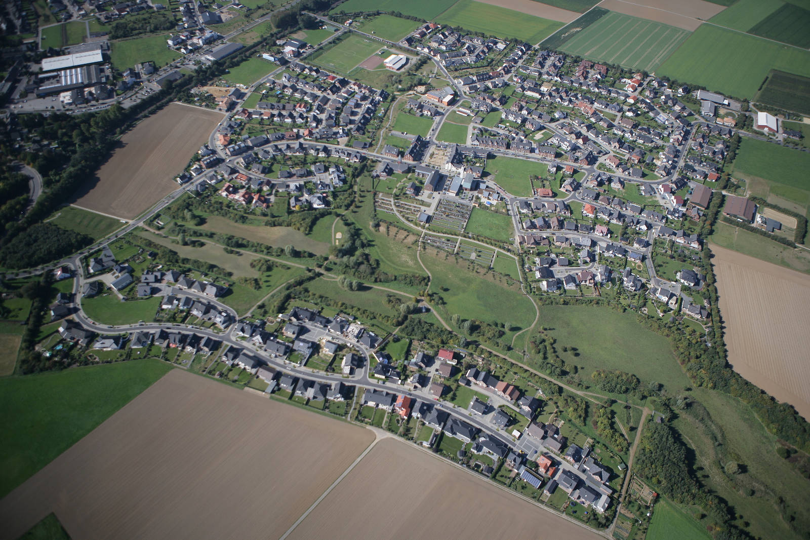 Luftaufnahme eines ländlichen Wohngebiets mit grünen Feldern und Straßen sowie Häusern.