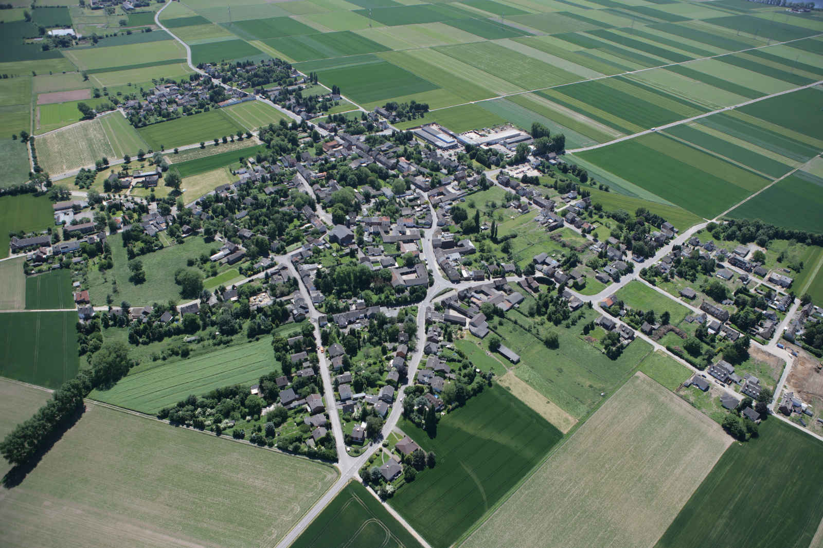 Luftaufnahme eines kleinen Dorfes umgeben von grünen Feldern und landwirtschaftlichen Flächen.