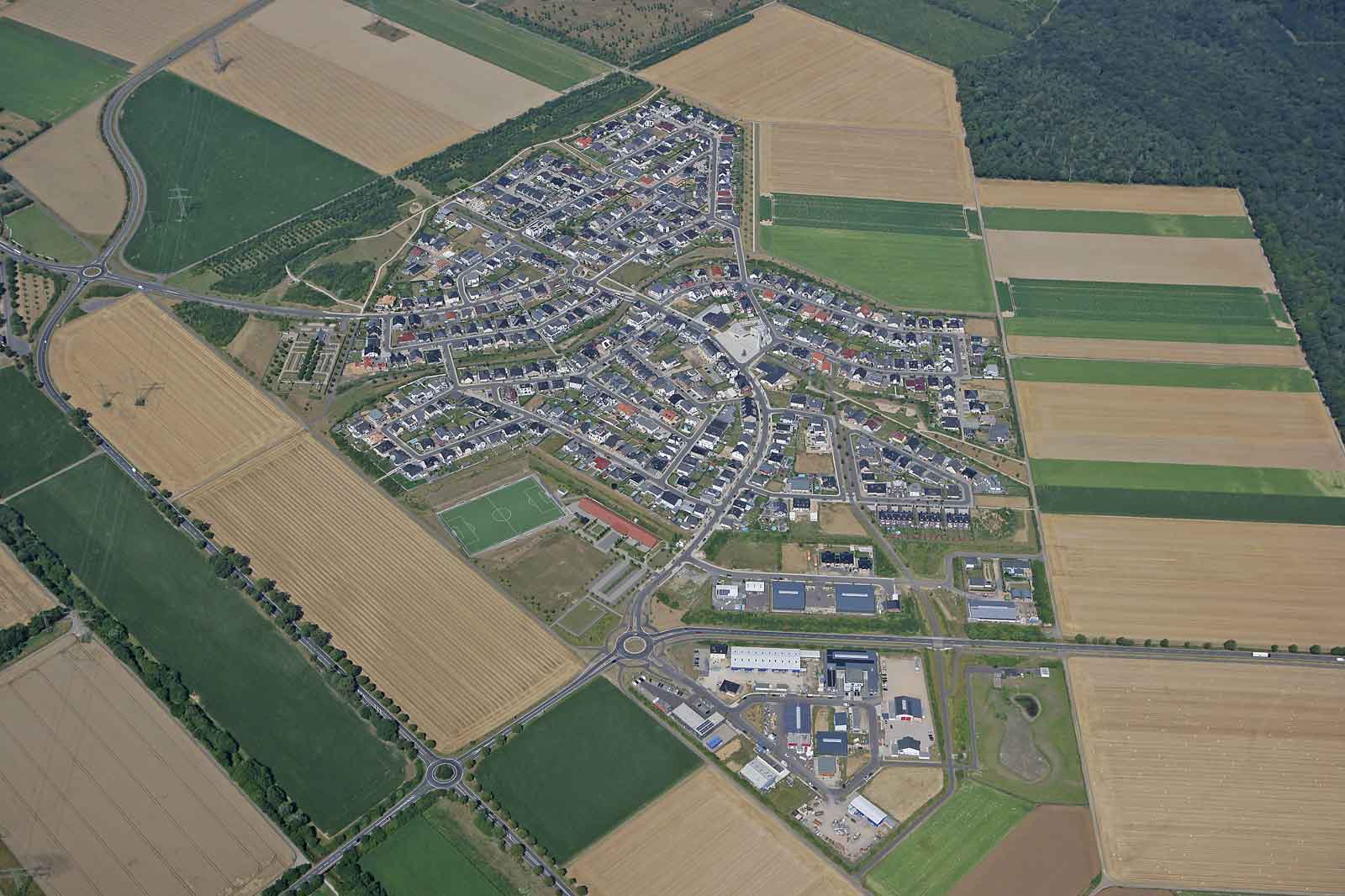 Eine Luftaufnahme eines Wohngebiets, umgeben von Feldern und Ackerland, mit Straßen und Häusern.