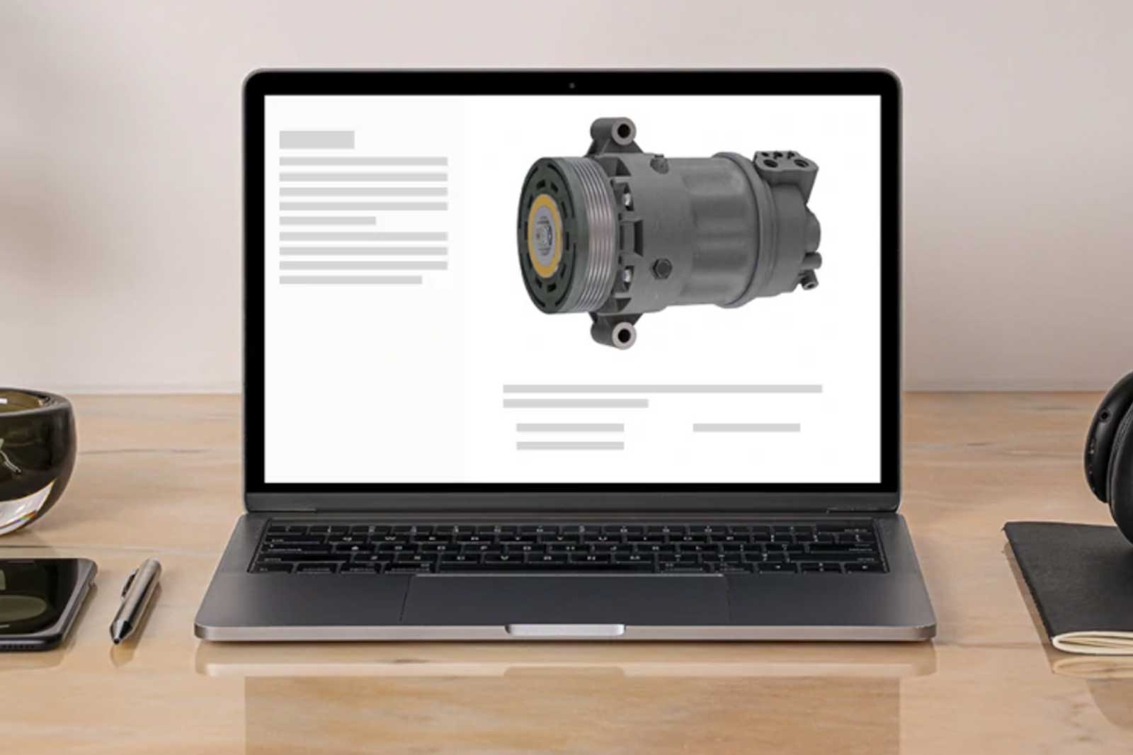 A laptop displays an automotive part, with a grey compressor prominently featured on a white background.