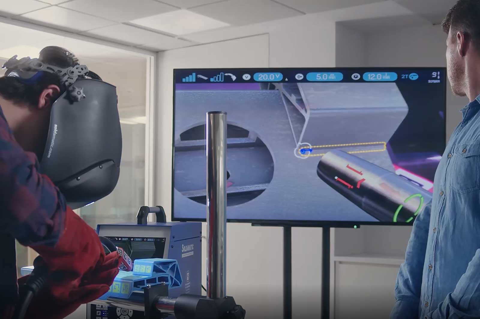 A welder operates advanced equipment while a screen displays instructions and information.