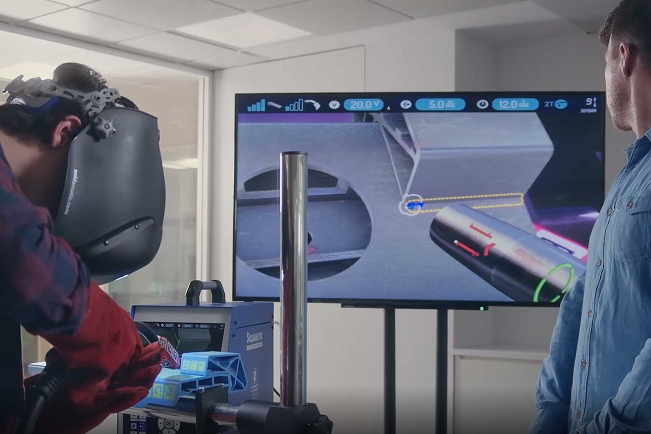 A welder operates advanced equipment while a screen displays instructions and information.