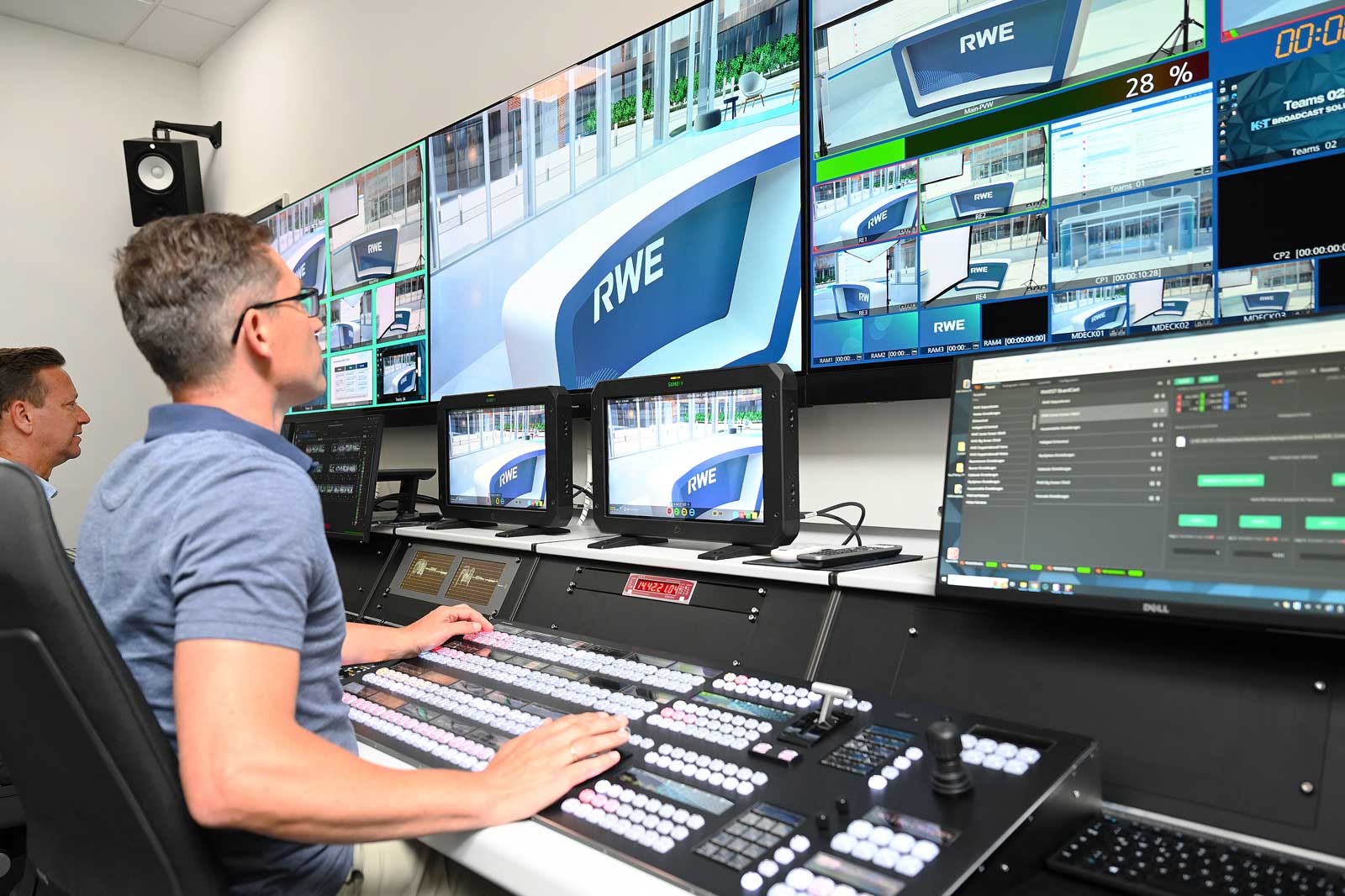 Ein Bediener steuert mehrere Monitore in einem Kontrollraum mit RWE-Logos, während er an einem professionellen Steuerpult arbeitet.