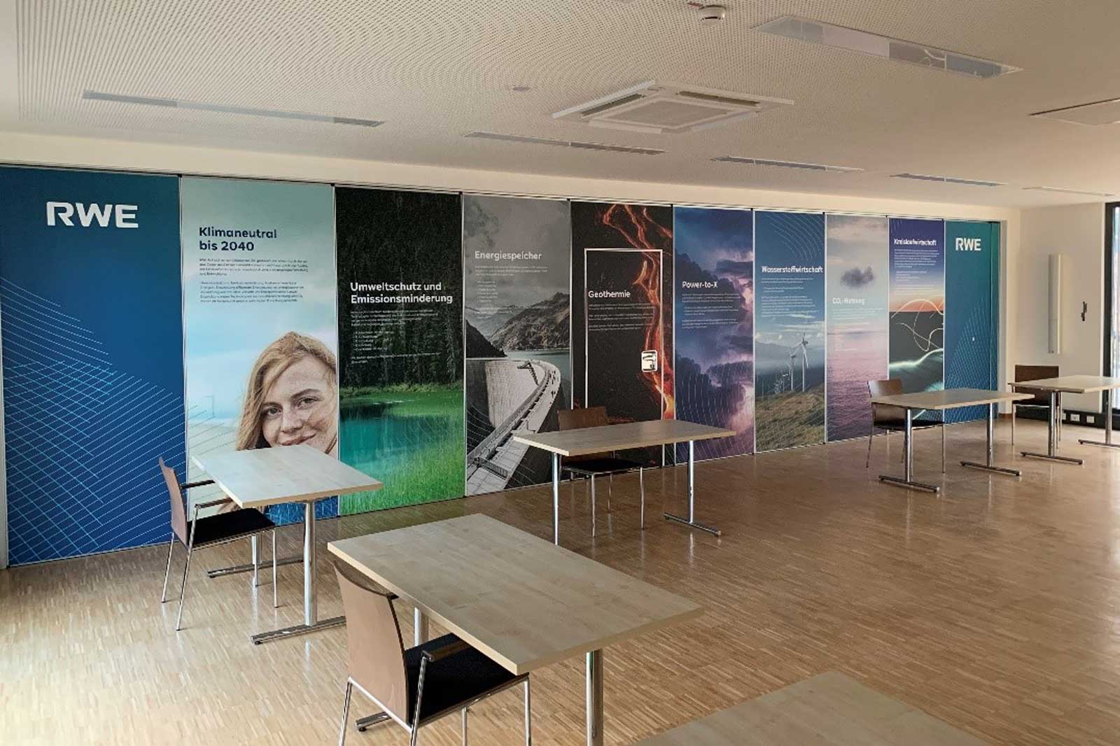 Ein Büroraum mit mehreren Tischen, an dessen Wänden informative Poster zu Nachhaltigkeit und Energielösungen hängen.